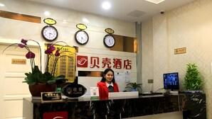 A hotel reception desk with clocks, a receptionist, and a sign with Chinese characters. - Shell Shanghai Pudong New District Zhongke Road Hotel (Shanghai)