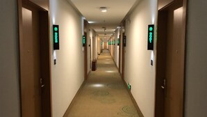 Un couloir d’hôtel avec des portes des deux côtés, chacune étant signalée par une plaque verte indiquant le numéro de la chambre.
