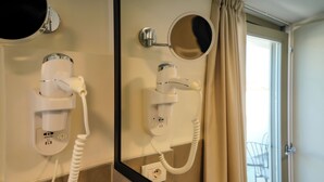 Une salle de bain équipée d’un sèche-cheveux fixé au mur, d’un miroir et d’une fenêtre avec un rideau.