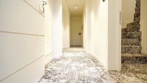 Un couloir avec un tapis à motifs, des murs blancs et un escalier recouvert d’un tapis à motifs.