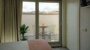 Une chambre d’hôtel avec un lit, une porte-fenêtre coulissante donnant sur un balcon, une petite table avec une chaise et une plante en pot.