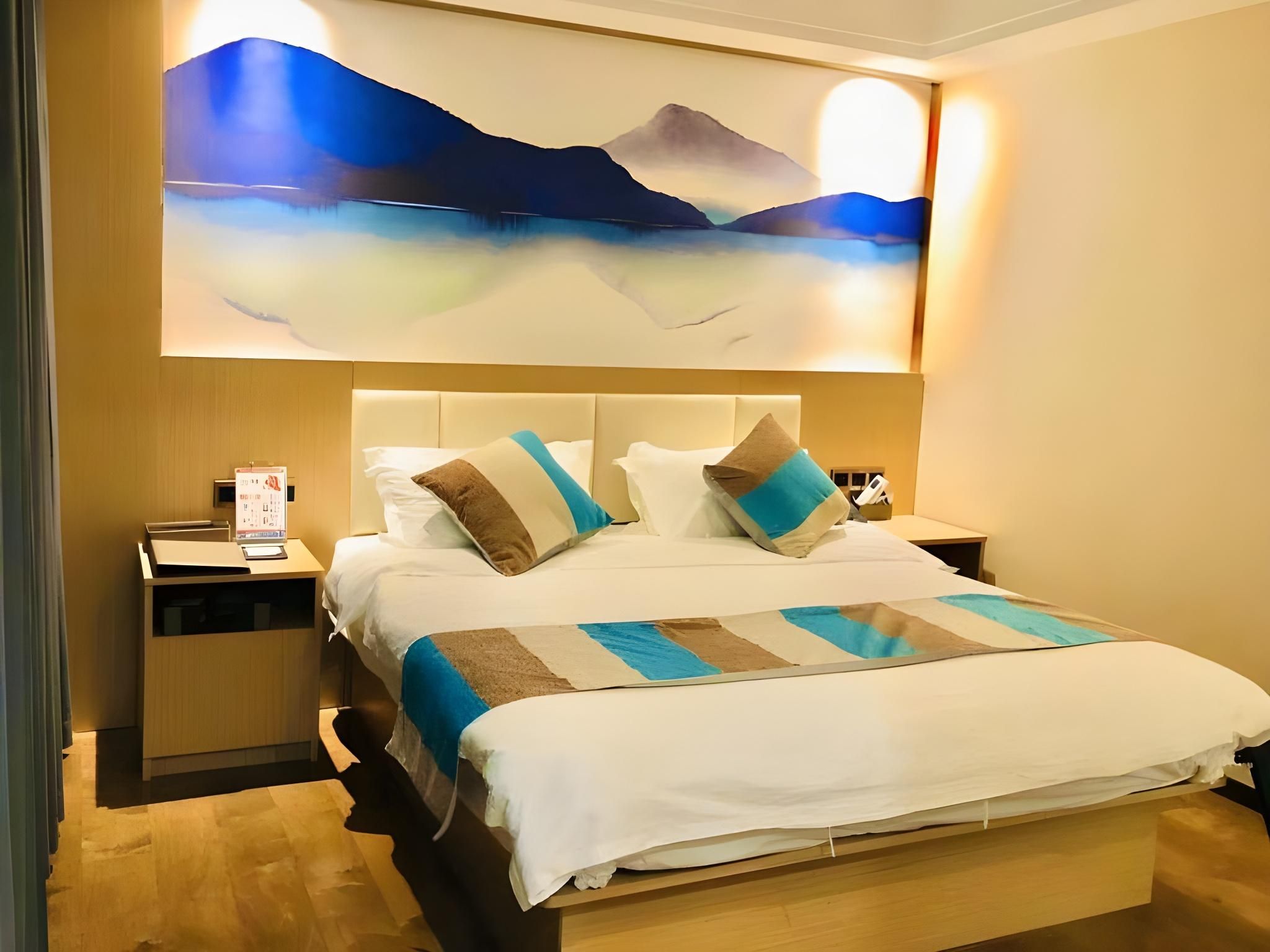 A hotel room with a bed, nightstands, a desk, and a large wall painting.