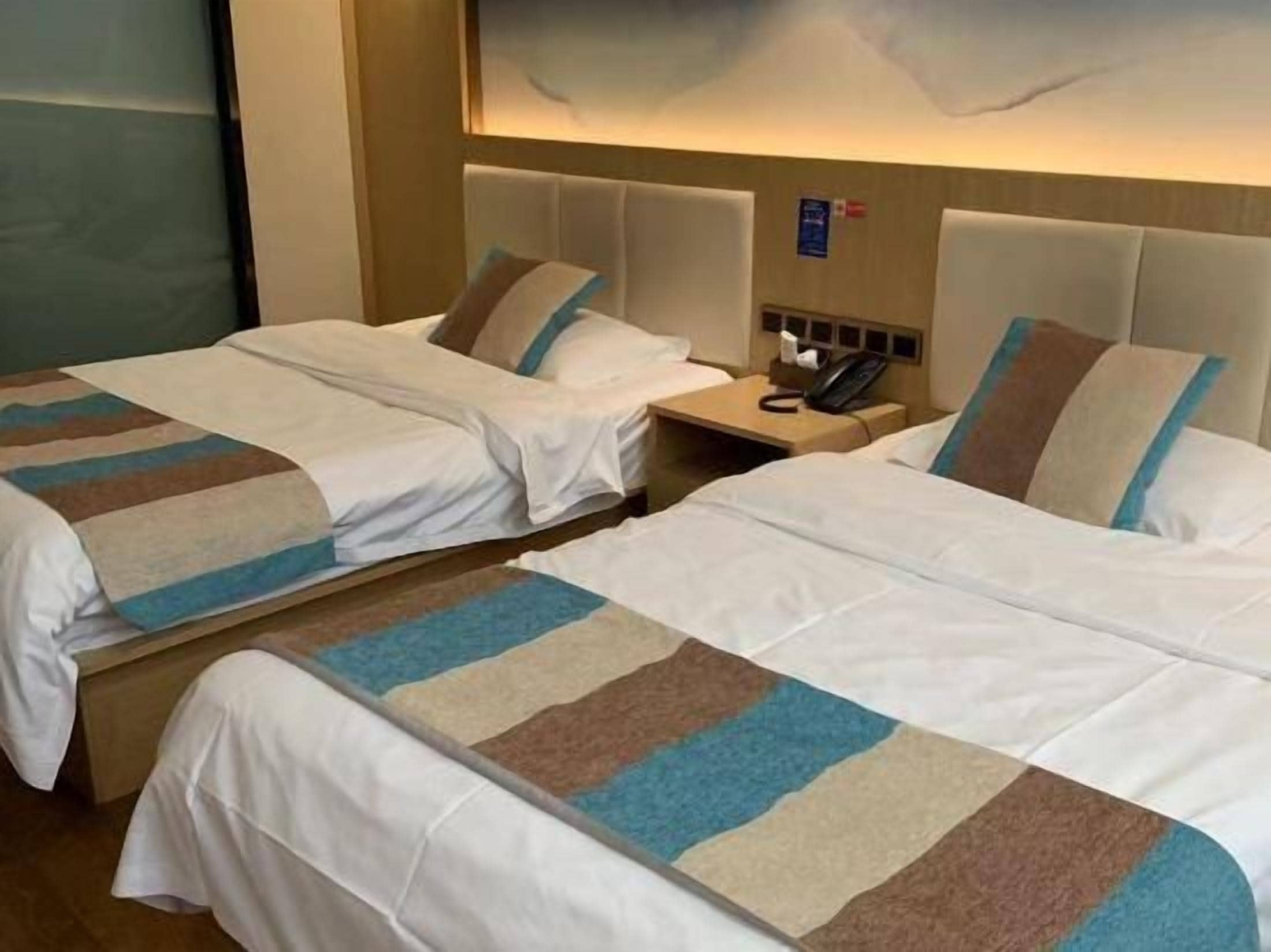 A hotel room with two beds, a nightstand with a telephone, and a wall-mounted light fixture.