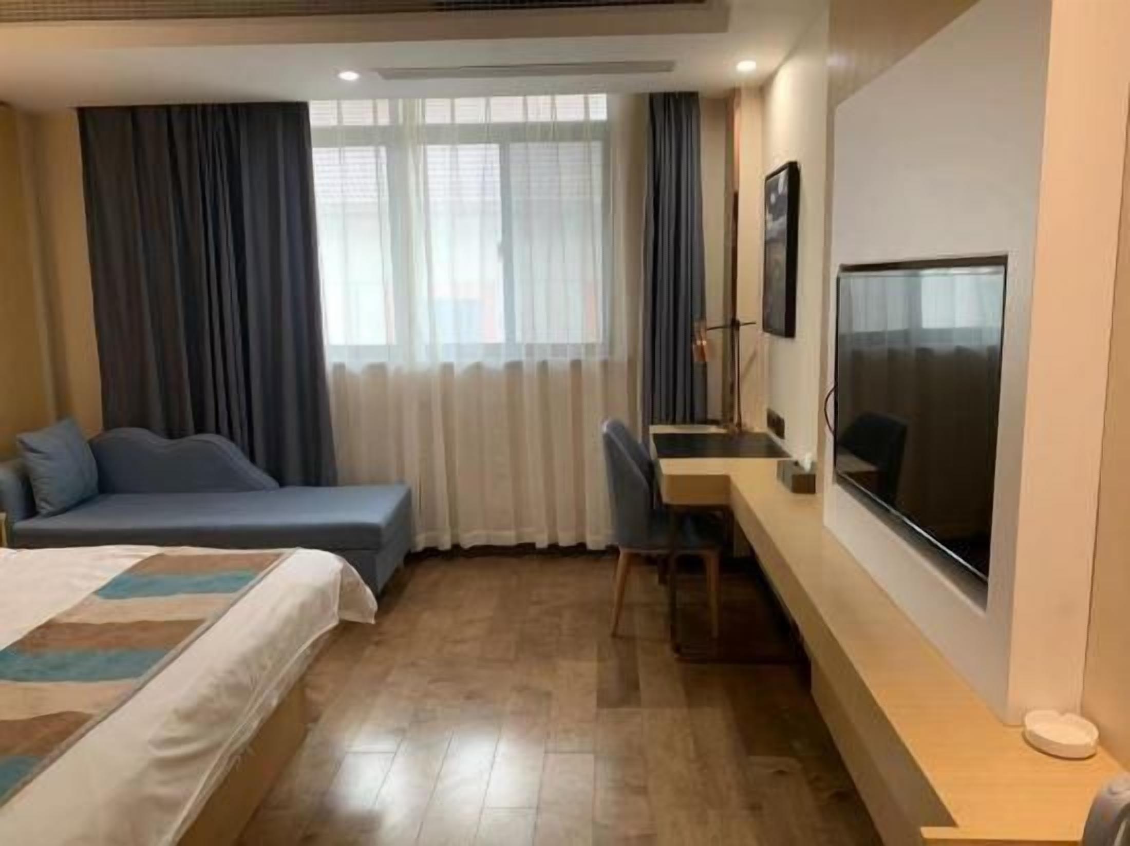 A hotel room with a bed, a desk, a chair, a TV, and a window with curtains.