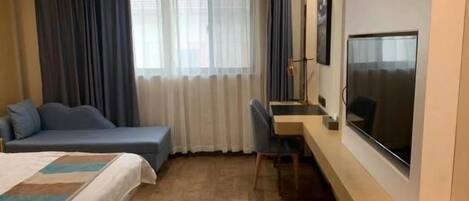 A hotel room with a bed, a desk, a chair, a TV, and a window with curtains.