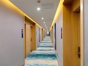 A hotel corridor with a long hallway, doors on both sides, and a patterned carpet.