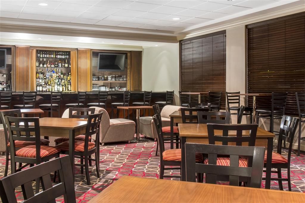 A hotel lobby with multiple seating areas, a bar with a variety of liquor bottles, and a large flat-screen TV mounted on the wall.
