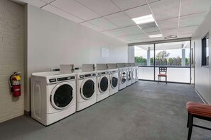 A laundry facility with multiple washing machines, a fire extinguisher, and a view through large windows.
