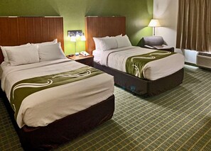 Une chambre d’hôtel avec deux lits, une table de chevet, une lampe et un climatiseur fixé au mur.