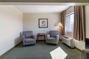 A hotel room with two armchairs, a small table, a lamp, a radiator, and a window with curtains.