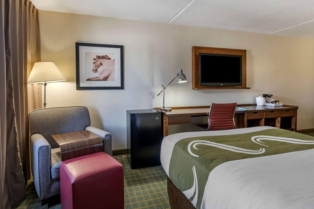 Ein Hotelzimmer mit Bett, Schreibtisch, Stuhl, Lampe, Fernseher und Kühlschrank.