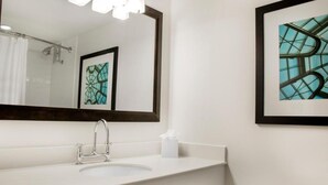 Une salle de bain moderne avec un grand miroir, un lavabo blanc et une œuvre d’art encadrée accrochée au mur.