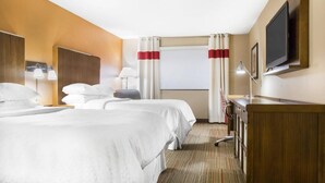 Une chambre d’hôtel avec deux lits, un bureau, une télévision et une fenêtre avec des rideaux.