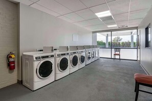 A laundry facility with multiple washing machines, a fire extinguisher, and a view through large windows.