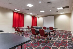 A conference room with tables, chairs, a projector screen, and red curtains.