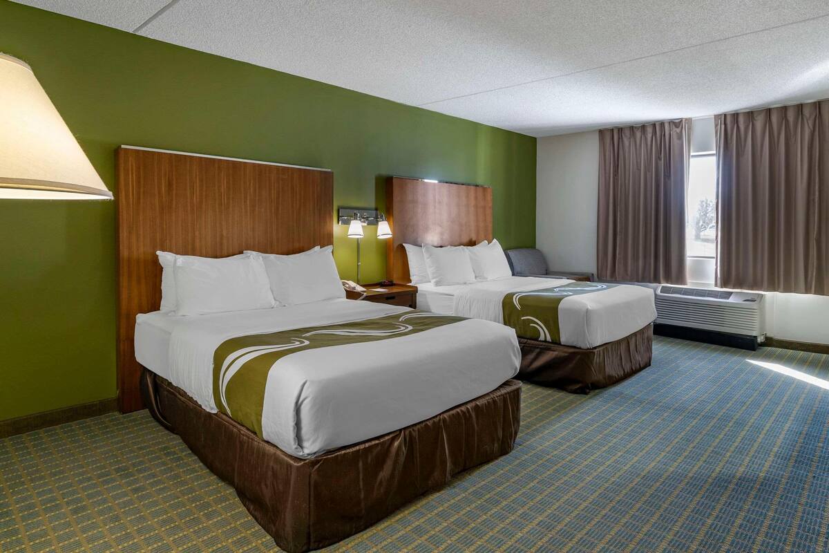Ein Hotelzimmer mit zwei Betten, grünen Wänden und einem gemusterten Teppich.