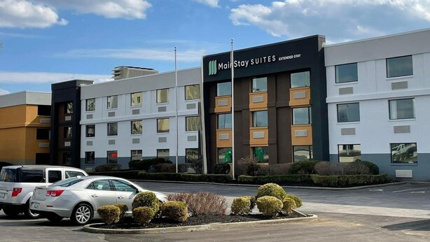 Un hôtel à plusieurs étages, une enseigne indiquant « MainStay Suites Extended Stay », et un parking rempli de voitures.
