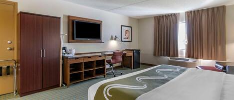 Una habitación de hotel con una cama, un escritorio con silla, un televisor, un armario y una ventana con cortinas.
