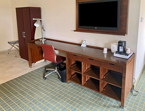 A hotel room with a wooden desk, a red office chair, a television, a coffee maker, and a small trash bin.