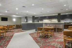 Un hall d’hôtel doté d’un comptoir d’accueil central, de plusieurs espaces de détente avec des tables et des chaises, d’un tapis à motifs et d’un sol carrelé.