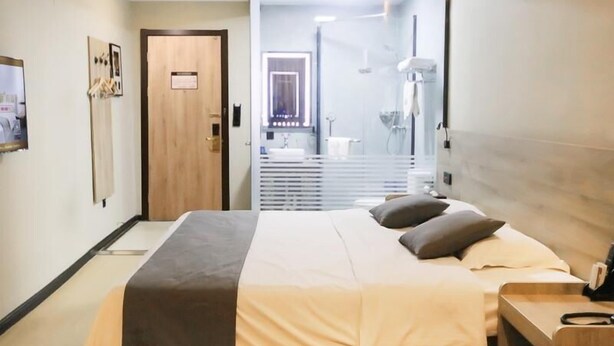 A modern hotel room with a large bed, bedside table, and a bathroom visible through a glass door. - Greentree Inn Zaozhuang Tengzhou Fuqian Road Longquan Square Business Hotel (Zaozhuang)