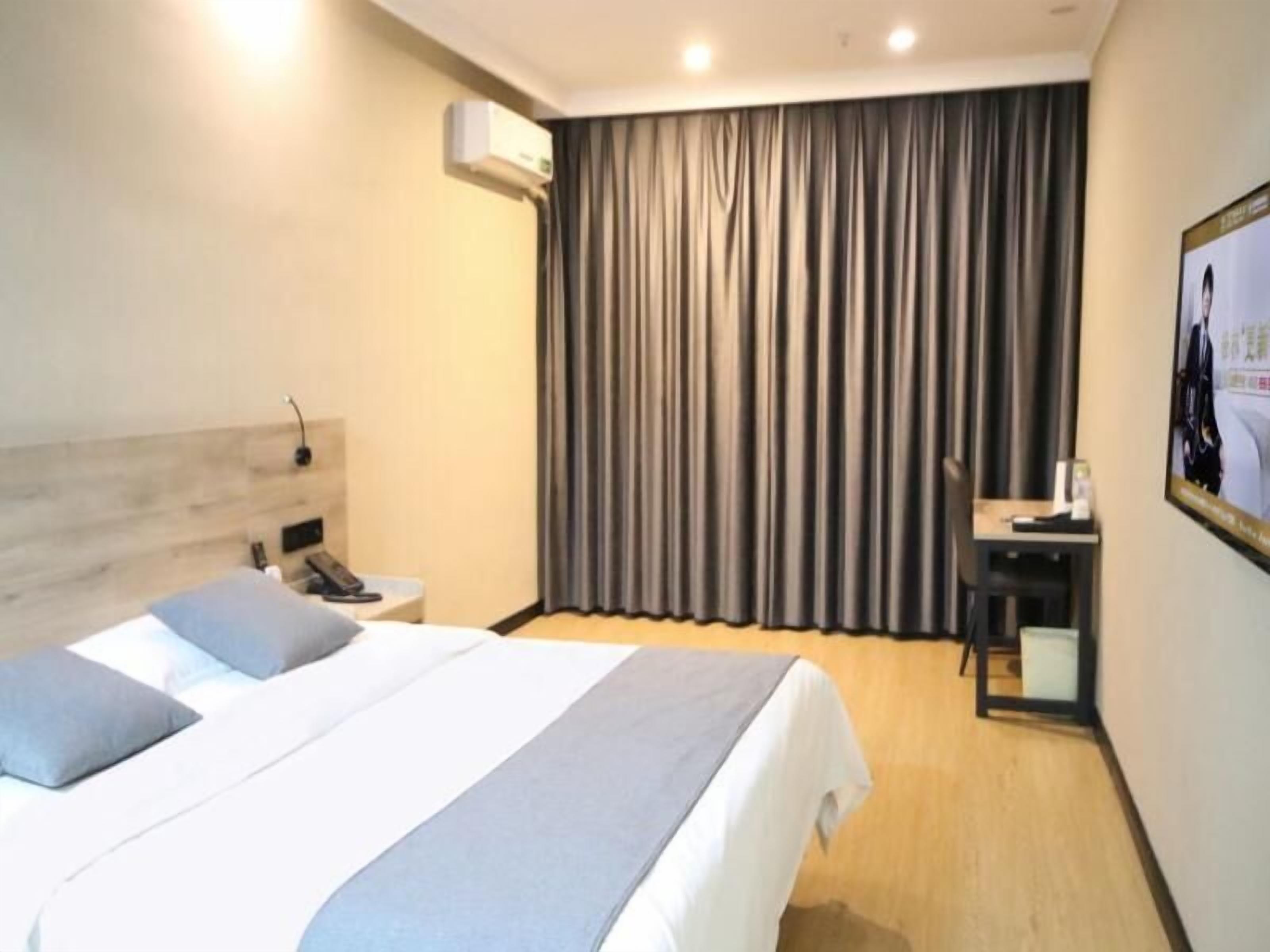 A hotel room with a bed, a desk, an air conditioning unit, and a curtain.