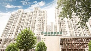 A hotel with multiple floors, a green sign with white text, and several parked cars in front. - Greentree Inn Zaozhuang Tengzhou Fuqian Road Longquan Square Business Hotel (Zaozhuang)