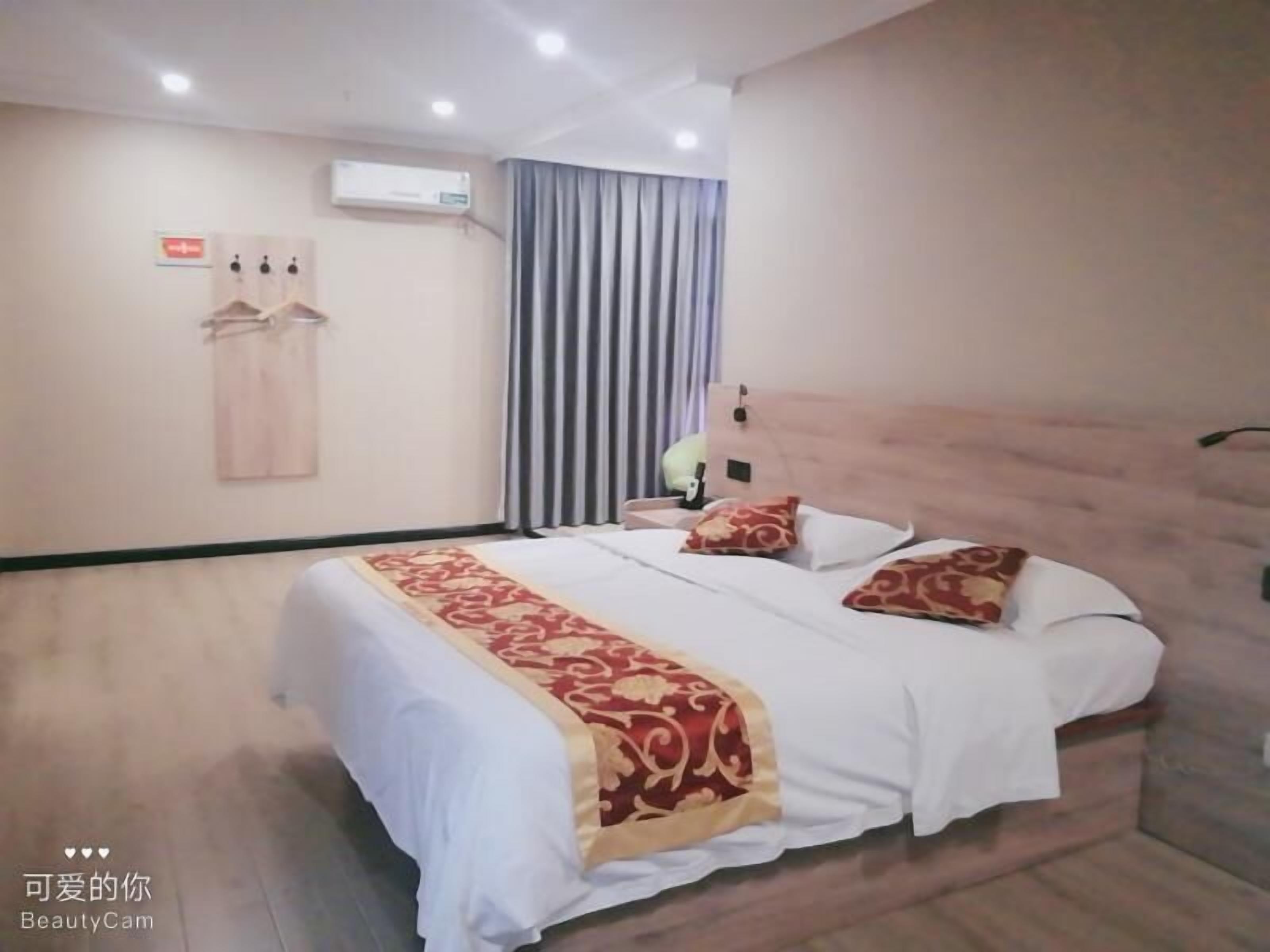 A hotel room with a large bed, a wooden headboard, a bedside table, a wall-mounted air conditioner, and a curtain.