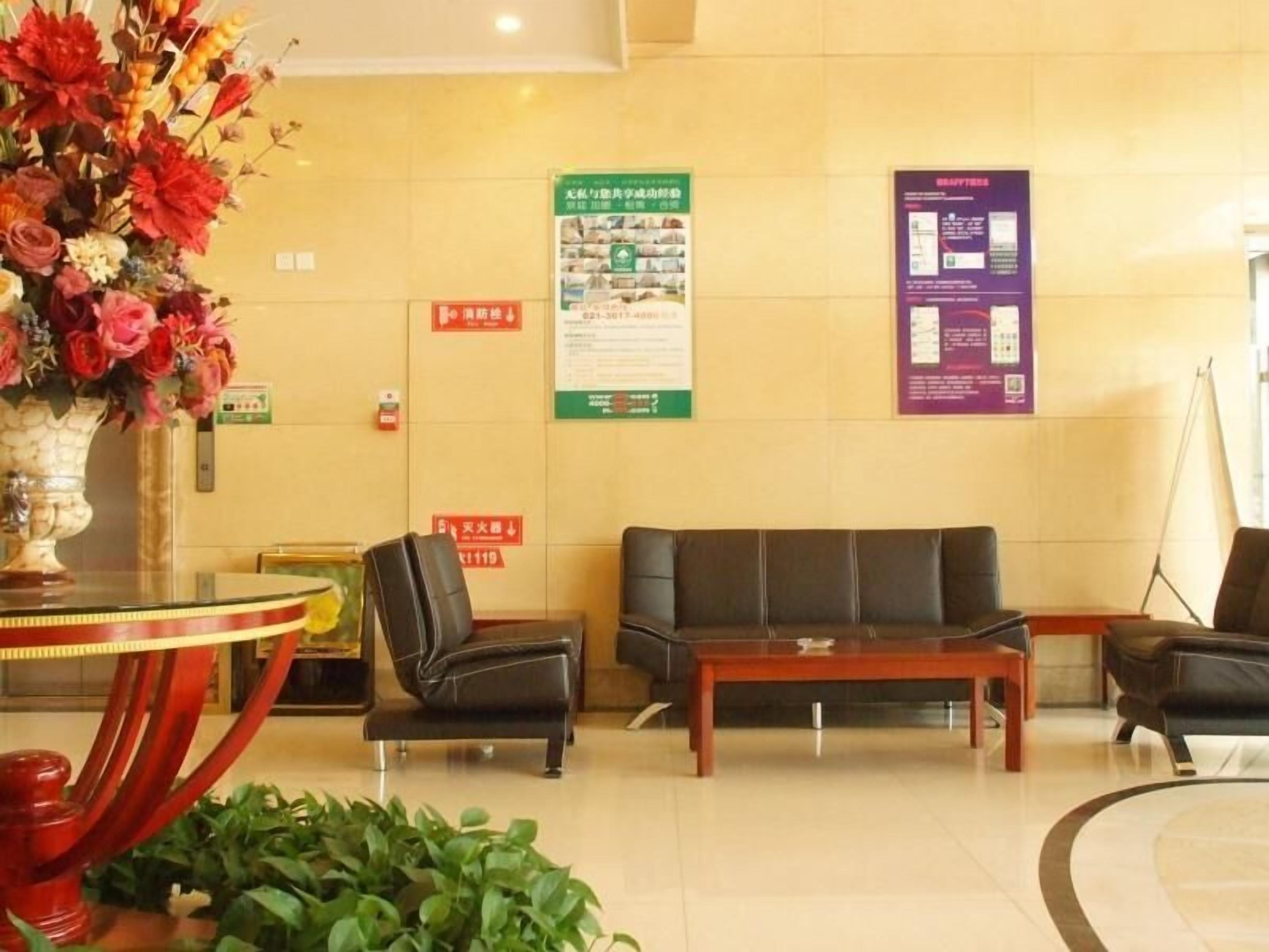 A lobby with a reception desk, a sofa, a coffee table, and a vase of flowers. There are informational posters on the wall and a fire alarm.