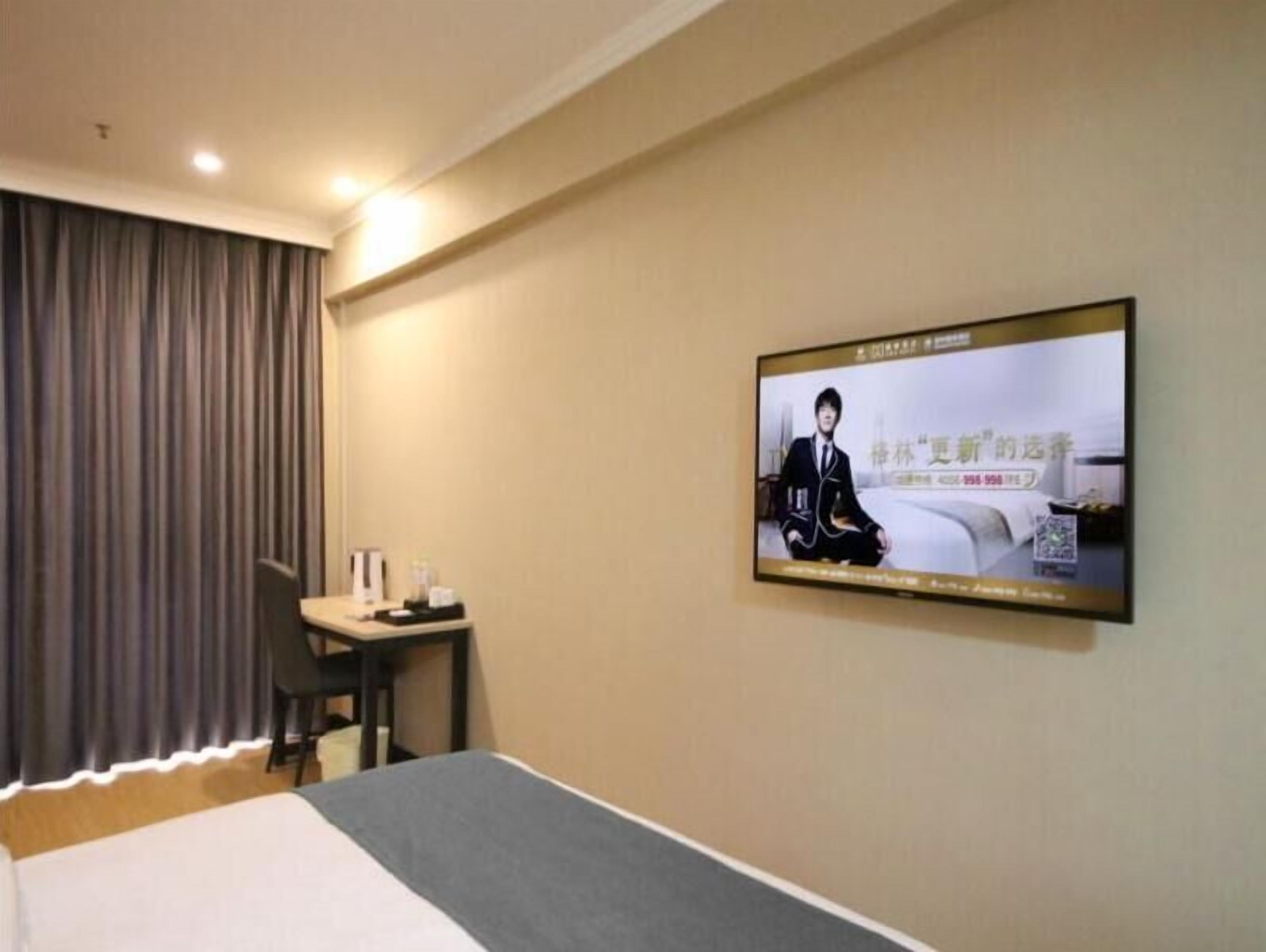A hotel room with a bed, a desk, and a television mounted on the wall.