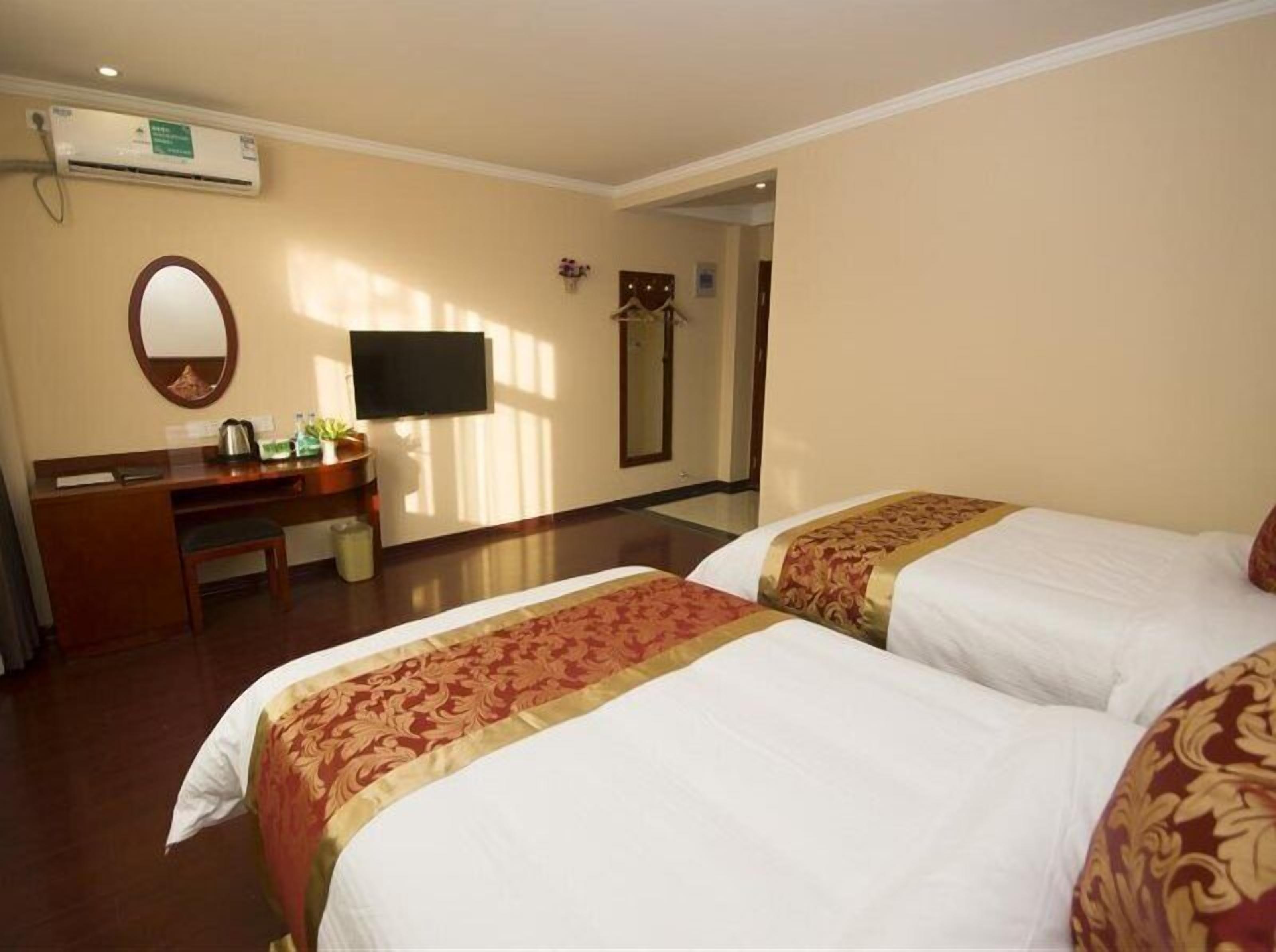 A hotel room with two beds, a desk, a mirror, and a television.