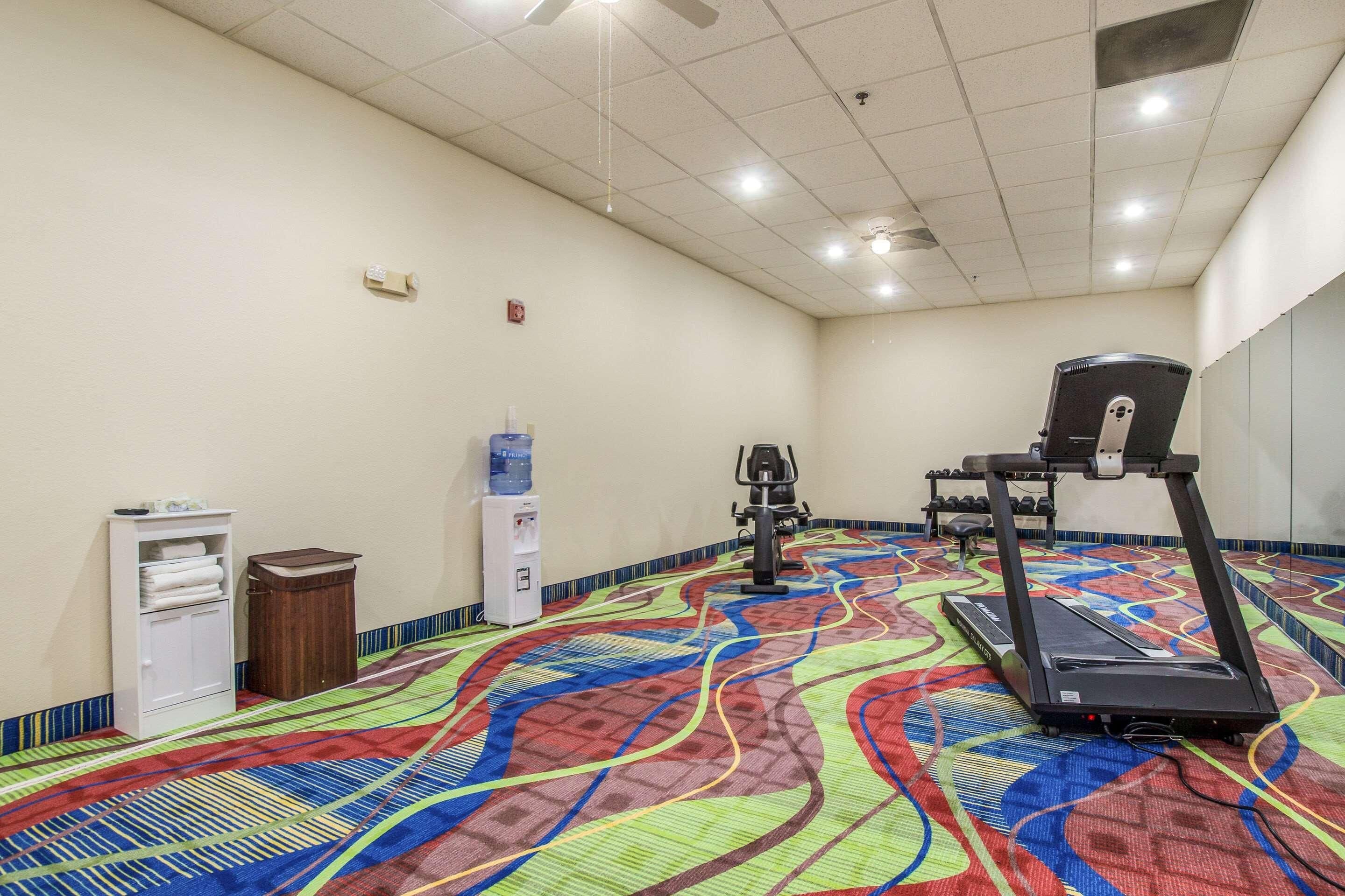 A gym with a colorful floor, a water dispenser, a trash bin, and exercise equipment.