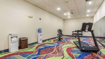 A gym with a colorful floor, a water dispenser, a trash bin, and exercise equipment.