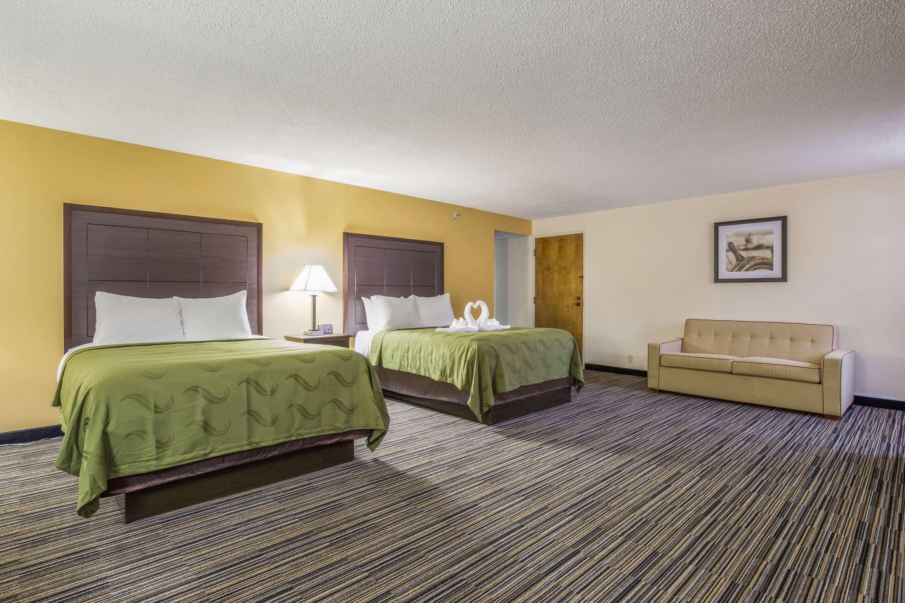 A hotel room with two beds, a sofa, and a carpeted floor.