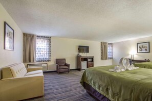 A hotel room with a large bed, a sofa, a desk with a television, and a chair.