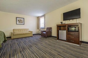 Habitación de hotel con sofá, sillón, televisor de pantalla plana, microondas y refrigerador pequeño.