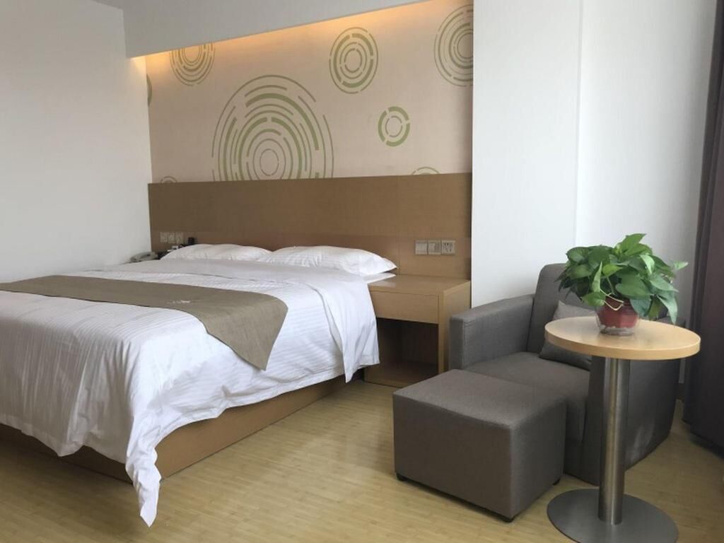 Een moderne hotelkamer met een groot bed, een nachtkastje, een kleine bank en een ronde tafel met een plant.