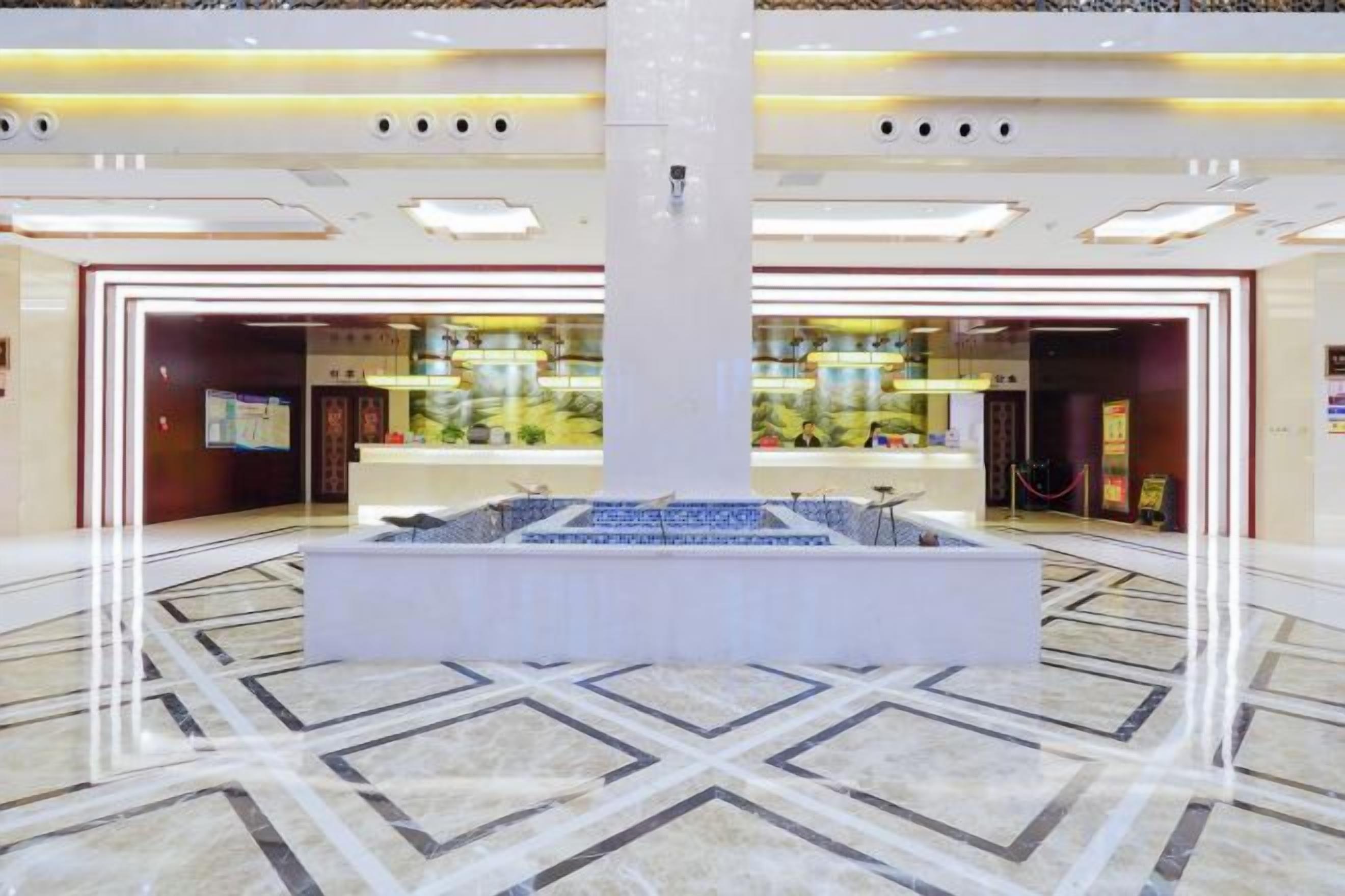 A hotel lobby with a central reception desk, a large pillar, and a patterned floor.