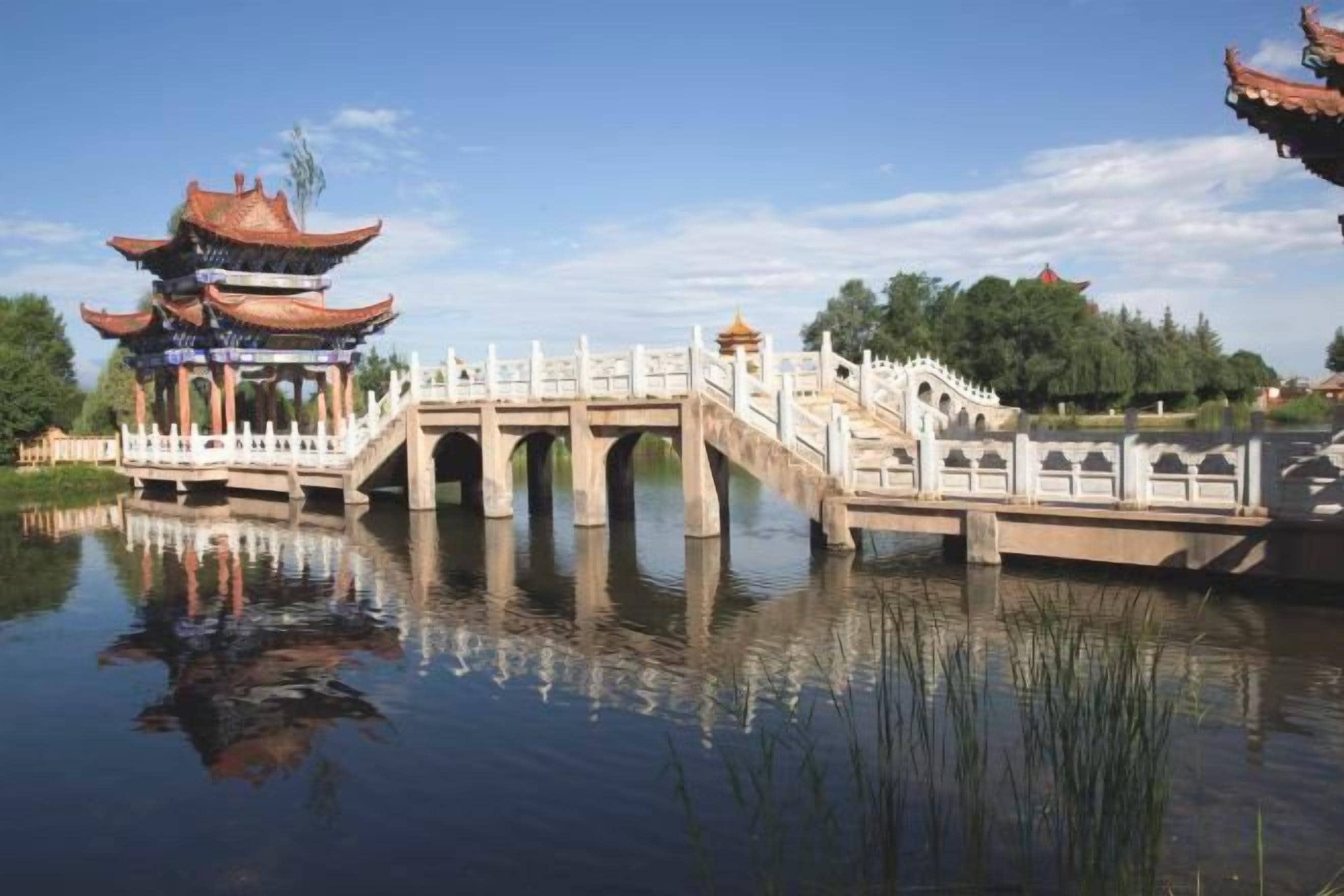 Ein traditioneller chinesischer Pavillon über ruhigem Wasser, verbunden durch eine Brücke mit weißer Brüstung.
