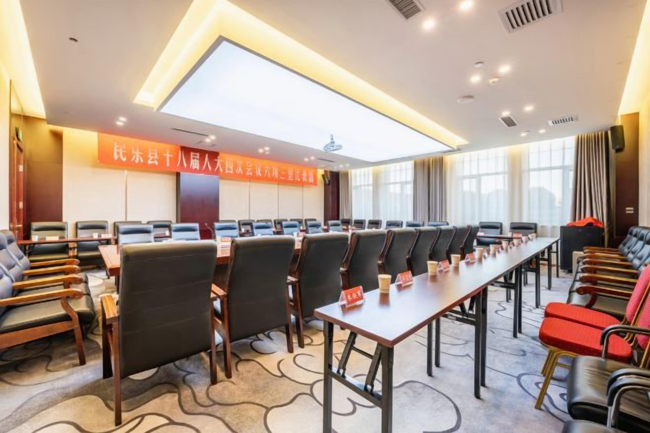 A conference room with a long table and multiple chairs, a large window, and a banner on the wall.
