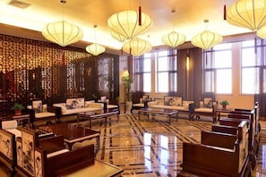 Um hall de hotel com decoração tradicional, incluindo paredes padronizadas, mobiliário de madeira e luminárias pendentes.