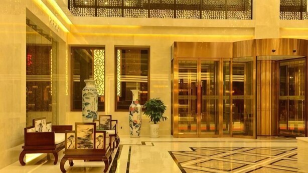 A lobby with a marble floor, a reception desk, a large vase, and a glass elevator. - Min Le Long Xin Hotel (Minle)
