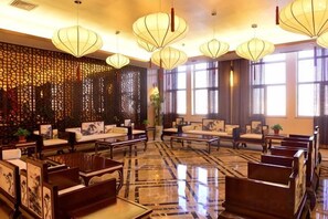 A hotel lobby with seating arrangements, large windows, and decorative lighting fixtures. - Min Le Long Xin Hotel (Minle)