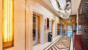 A hallway with a geometric patterned floor, a decorative wall with a lattice design, and a circular wall-mounted light fixture. - Min Le Long Xin Hotel (Minle)