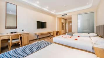 A hotel room with a desk, a bed with rose petals, a TV, and a large window.