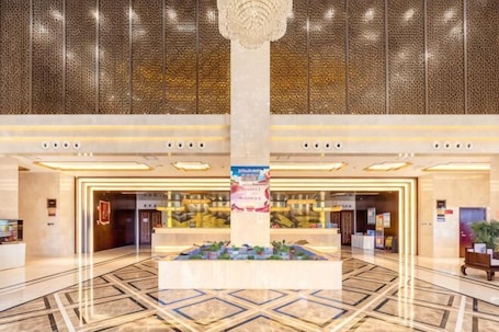 A spacious lobby with a central column, a reception desk, and a patterned ceiling.. Min Le Long Xin Hotel