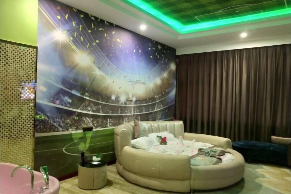 Una habitación con un mural grande de un estadio, un sofá beig color crema, una mesita redonda y un lavamanos rosa.