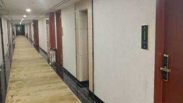 A hotel corridor with a carpeted floor, doors, and a wall-mounted control panel.