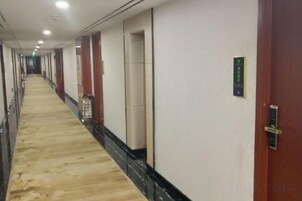 Un pasillo de hotel con piso alfombrado, puertas y un panel de control en la pared.
