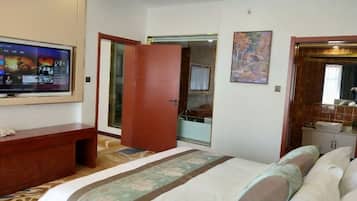 A hotel room with a bed, a TV mounted on the wall, a wooden desk, and a bathroom visible through an open door.